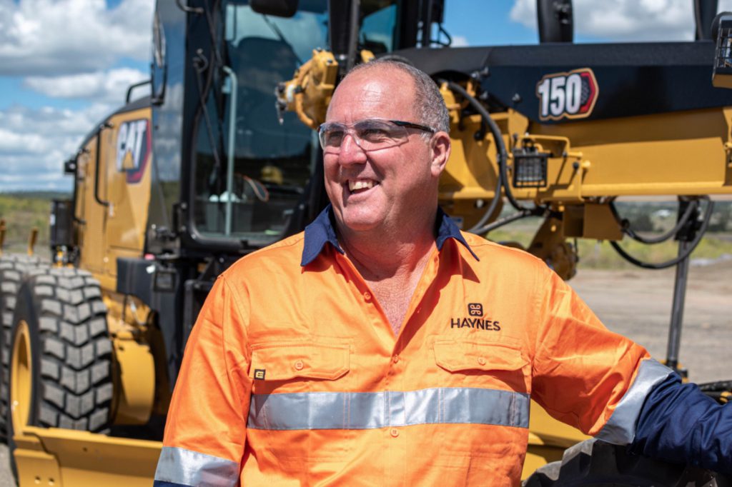 Smiling civil construction work in front of CAT grader